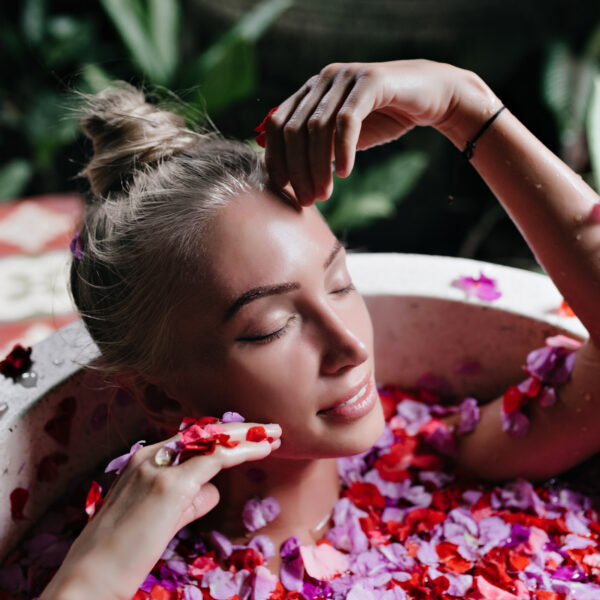 Close up photo attractive tanned woman chilling bath full rose petals indoor overhead shot refined blonde female model enjoying spa with gently smile 600x600