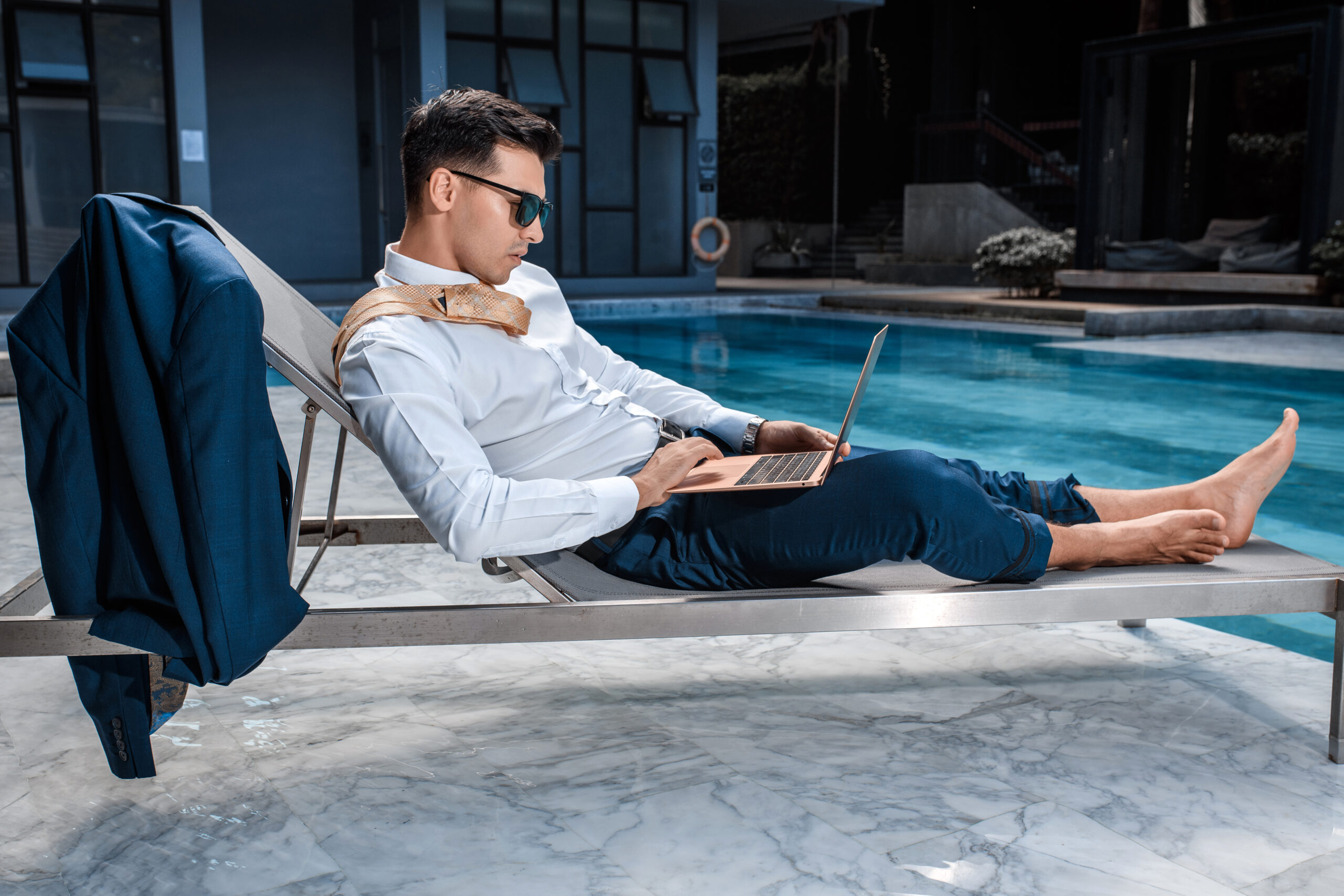Fashion photo smart man with laptop relaxing sun lounger near pool scaled