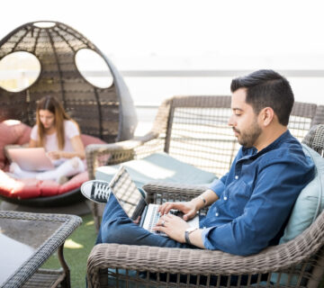 Handsome young latin man sitting armchair using laptop with female colleague background 360x320